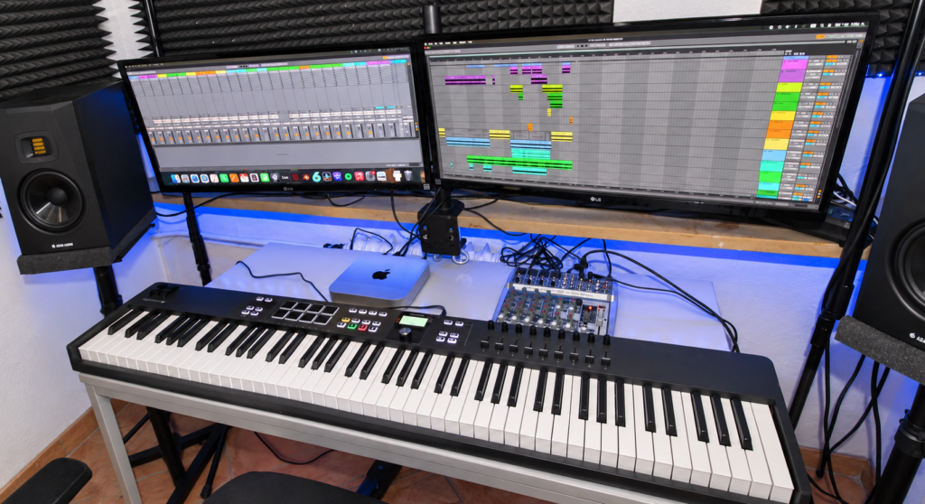 Nahaufnahme des Musikproduktionsarbeitsplatzes mit Keyboard, zwei Monitoren und Mischpult